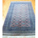 A Persian Bokhara rug with repeating motifs on a muted pink field