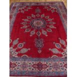 A signed Persian Mashad carpet, having a floral medallion on a plain red field