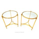 A pair of circular section occasional low tables with plate glass tops raised on gold coloured frame