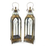 A pair of large storm lanterns with rounded arched glazed sides and a gold coloured finish