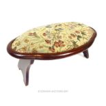 An oval fruit wood footstool, with floral needlepoint upholstery, raised on end supports