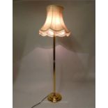 A brass standard lamp with an ivory coloured shade, raised on a circular base