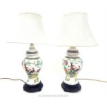 A pair of Chinese style ceramic table lamps with shades, the lamps decorated with peacocks