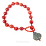 A necklace of red beads with jade style clasp in the form of the Buddha; 58cm long.