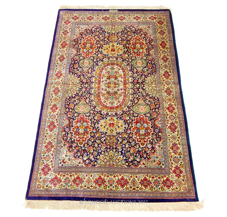 A signed Persian silk Qum rug, with a central medallion on a midnight blue field, profusely