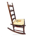 A ladder back fruitwood rocking chair, with floral needlepoint upholstered seat