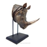 A bronzed resin sculpture of a rhino's head, raised on a black presentation stand