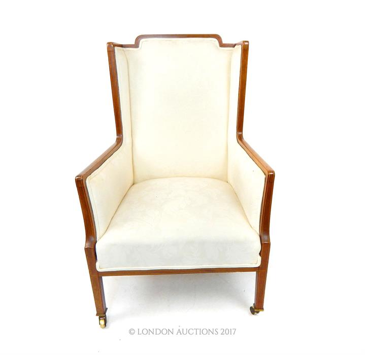 An Edwardian mahogany wing armchair with walnut frame and boxwood inlays and cream upholstery.