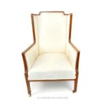 An Edwardian mahogany wing armchair with walnut frame and boxwood inlays and cream upholstery.