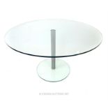 A contemporary circular glass table, raised on a brushed steel stem