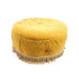 A circular pouffe upholstered in mustard fabric