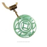 A Chinese, green, circular, carved jade pendant on cream leather thonging