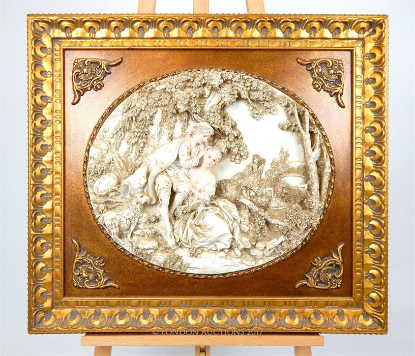 An oval decorative plaque depicting young lovers in relief, in a gilt frame