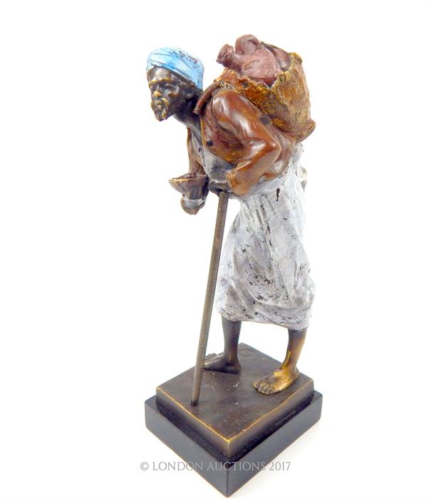 A painted bronzed metal figurine of an Asian gentleman carrying water; indistinctly signed base;