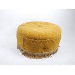 A circular pouffe upholstered in mustard fabric