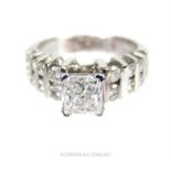 A diamond ring with princess cut central stone and brilliant cut stones to its shoulders; in total