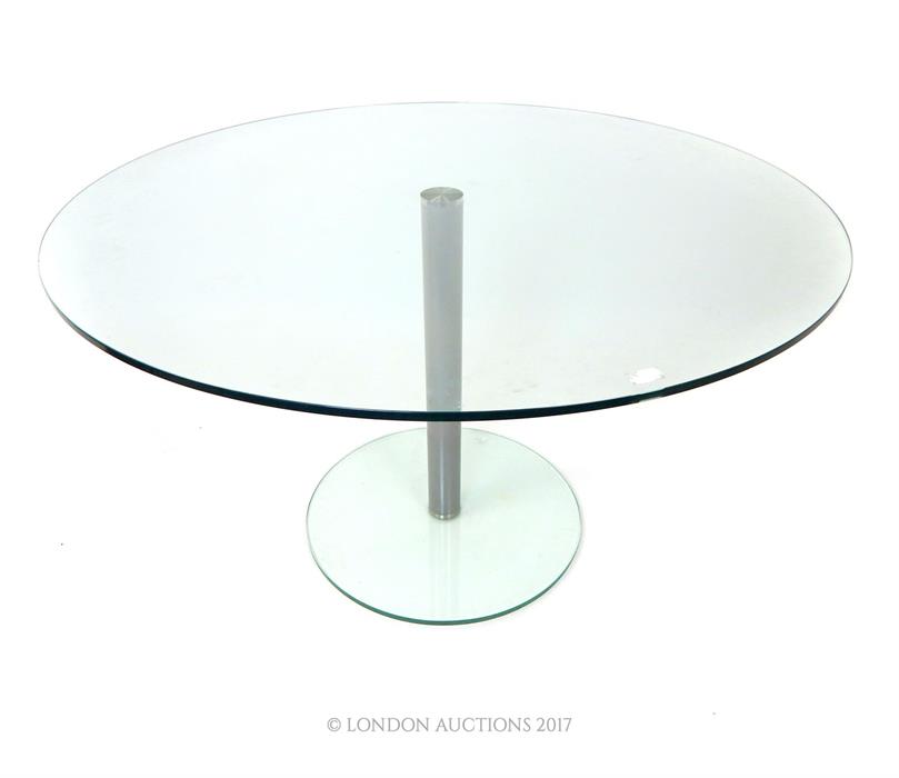 A contemporary circular glass table, raised on a brushed steel stem