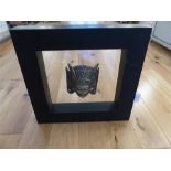 A framed white metal Indian mask