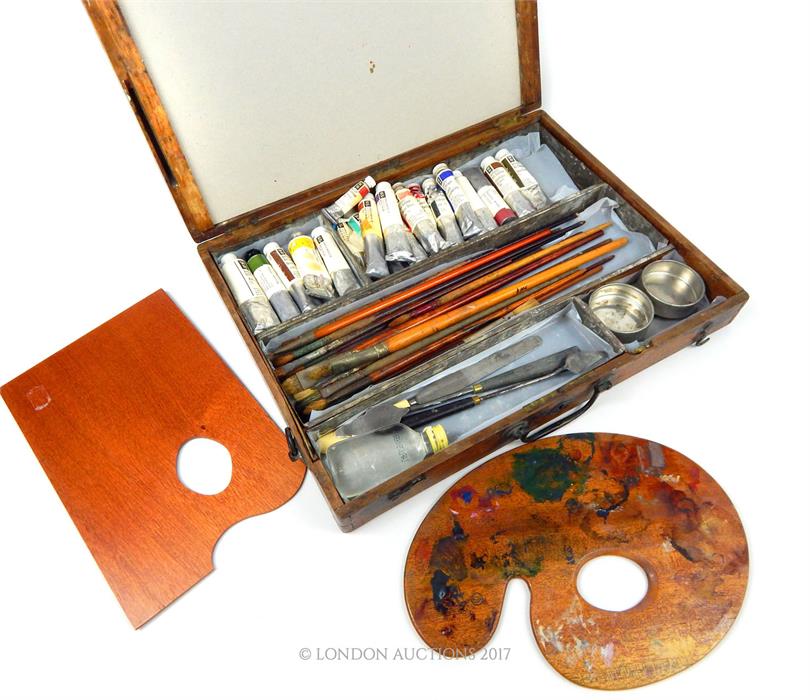 A vintage mid 20th century wooden paint box with oil paints, brushes and two palette knives along