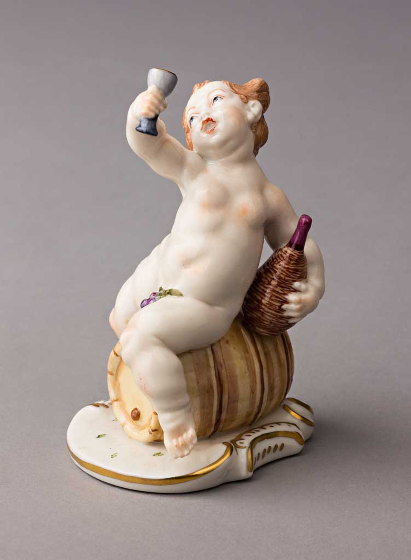 Putto als Bacchant, auf Weinfass sitzend. Polychrom staffierte Figurine. Modell Franz Anton