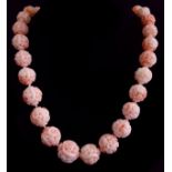 A rare graduated row of thirty one finely carved angel skin coloured coral beads, each spherical