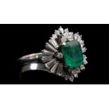 An emerald and diamond ring, the central emerald cut stone within a diamond ballerina setting, of