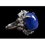 A cabochon sapphire and diamond ring set in white metal, the central domed stone within florets