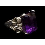 An amethyst and diamond dress ring, the central stone flanked by ribbon bows of brilliant and