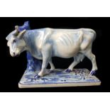 A tin glaze dairy advertising figure of a cow before a short tree stump, blue and white