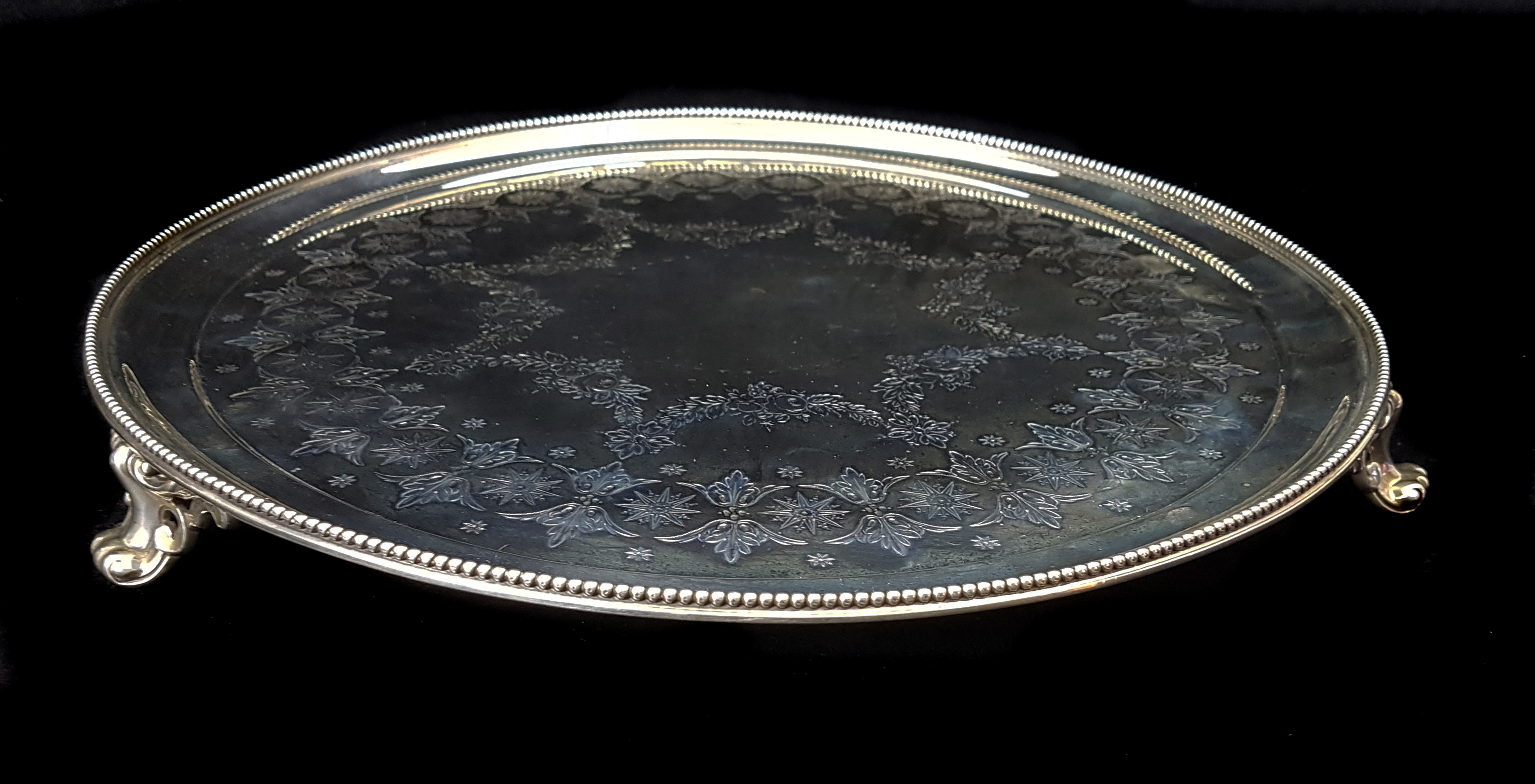 A circular silver salver, decorated with summer flower swags with a stiff leaf and star border,