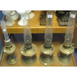 Four brass pedestal oil lamps with clear glass chimneys.