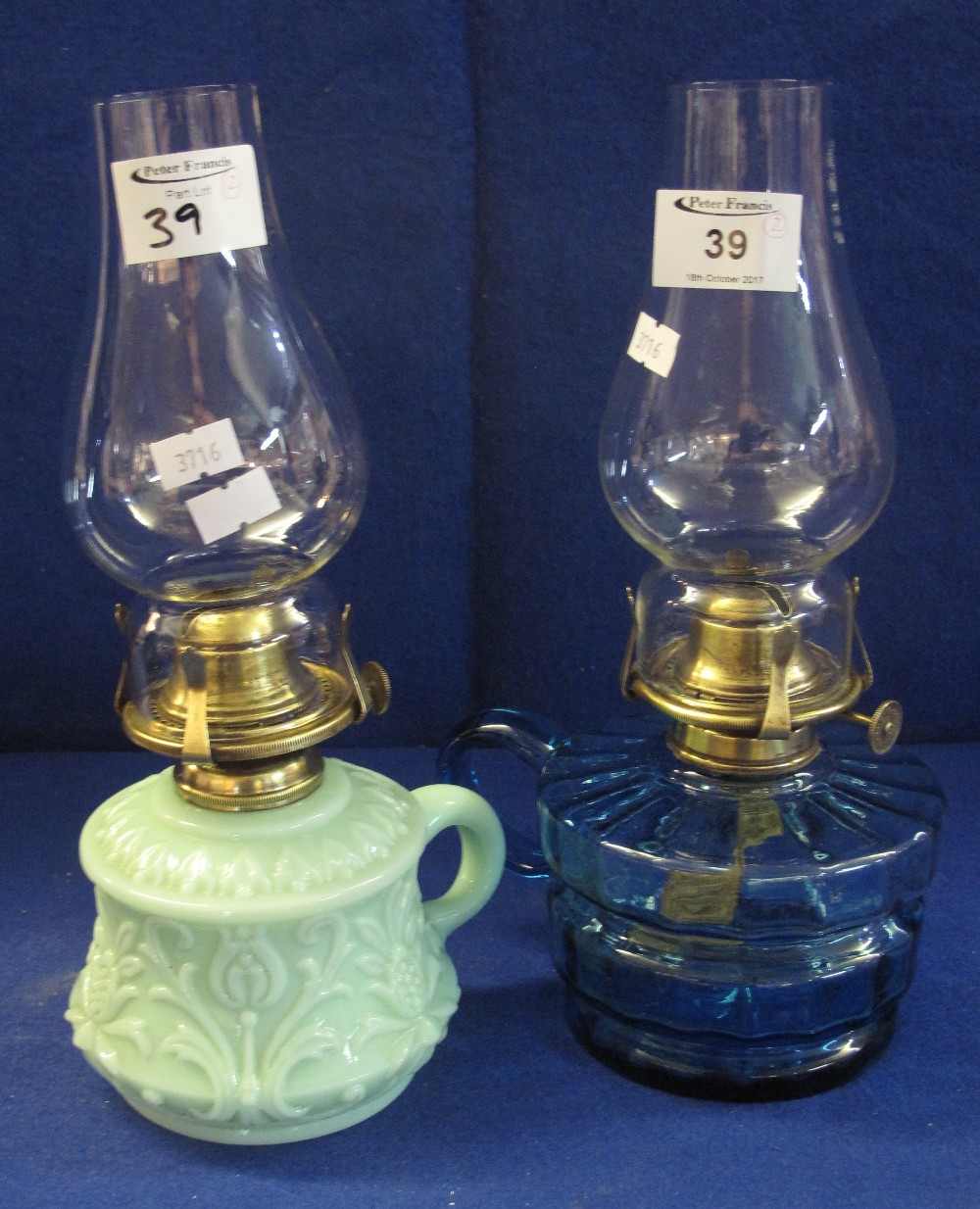 Two similar single oil burner chamber stick lamps, one blue glass, the other green slag type glass.