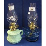 Two similar single oil burner chamber stick lamps, one blue glass, the other green slag type glass.