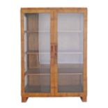 An Art Deco revival blonde walnut veneered display unit with two doors enclosing solid wood shelves.