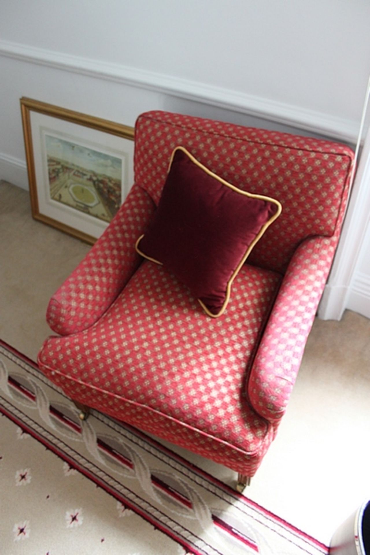 A pair of armchairs upholstered in red fabic with repeating red check pattern with base frill