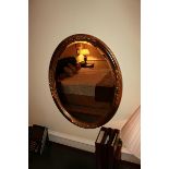 A mahogany oval carved wood bevel mirror with antiqued accents to the floral relief
