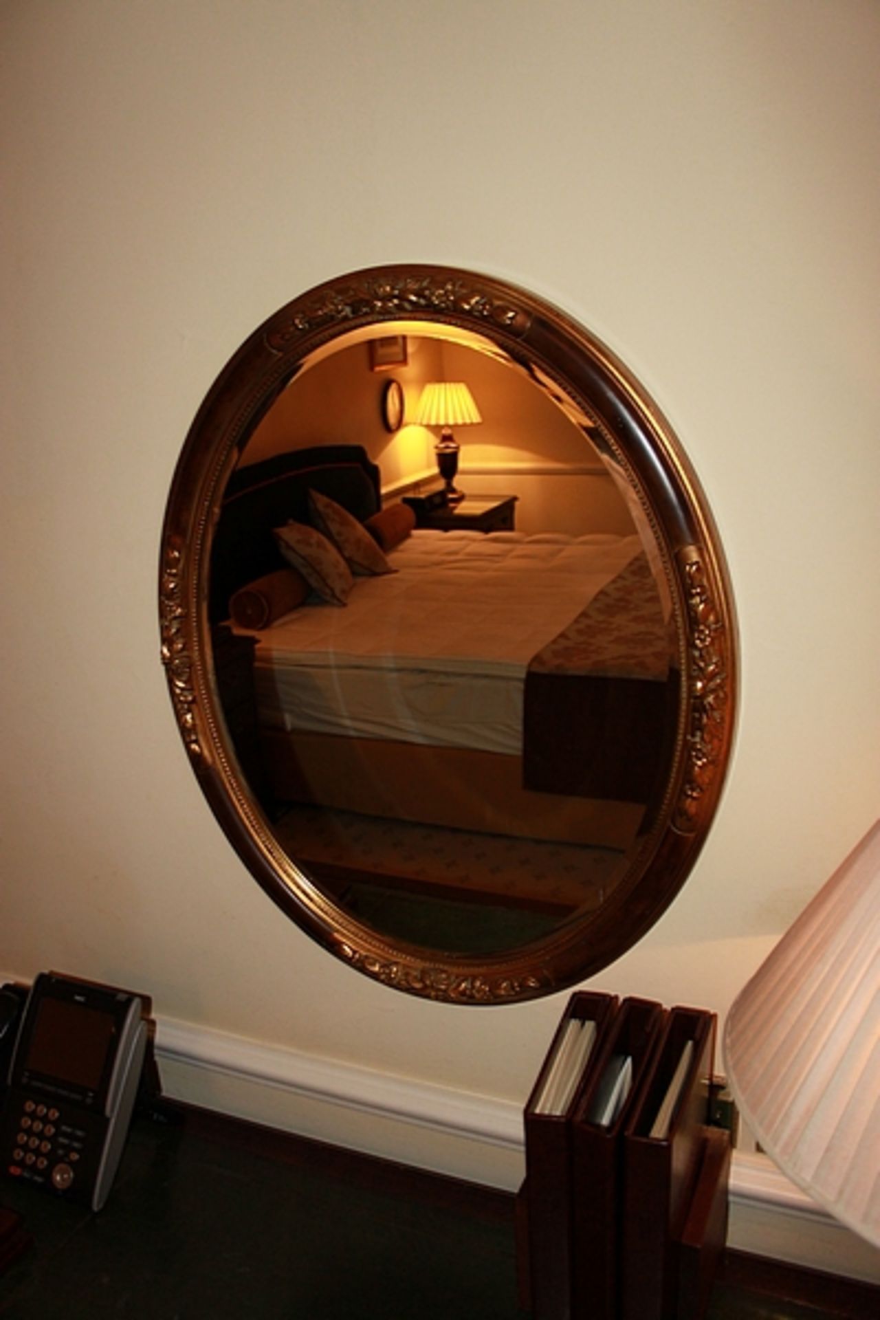 A mahogany oval carved wood bevel mirror with antiqued accents to the floral relief