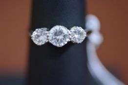 A white metal three stone graduated diamond ring mounted in open work claw setting, centre stone