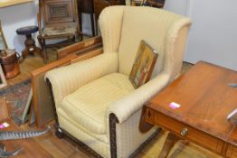 An early 20th century wing armchair with a scroll and gadroon carved frame, raised on ball and