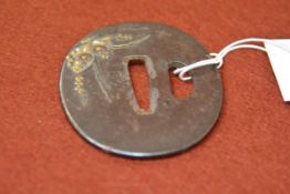 A Japanese iron tsuba, of shaped oval form, with shakudo decoration to one side of a floral spray.