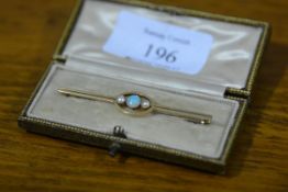 An early 20th century 15ct gold bar brooch set with an opal flanked by a pair of seed pearls, cased.