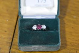 A three stone ruby and diamond ring, the central round-cut ruby claw-set between a pair of round