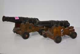 A pair of cast iron model cannon, each with ring-cast barrel and mounted on an oak gun carriage.