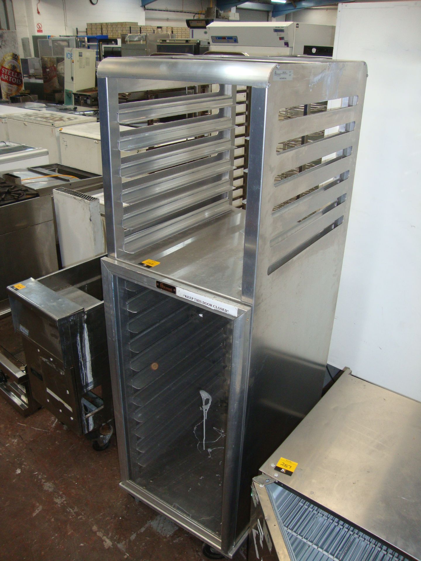 Mobile stainless steel unit comprising clear front storage compartment below and shelving for