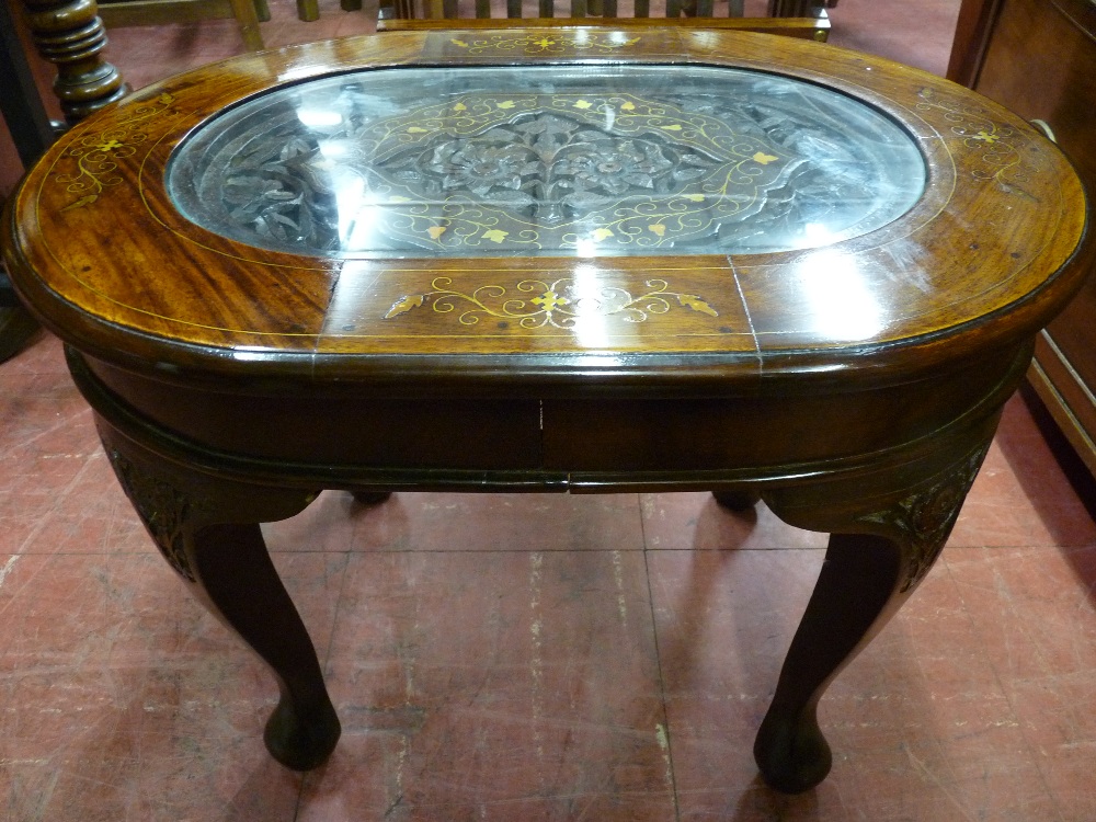 A MODERN HARDWOOD BRASS INLAID COFFEE TABLE, the oval top with central glass covered carved panel