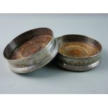 A PAIR OF WOODEN BASED CIRCULAR SILVER WINE COASTERS with garland decoration in the classical style,