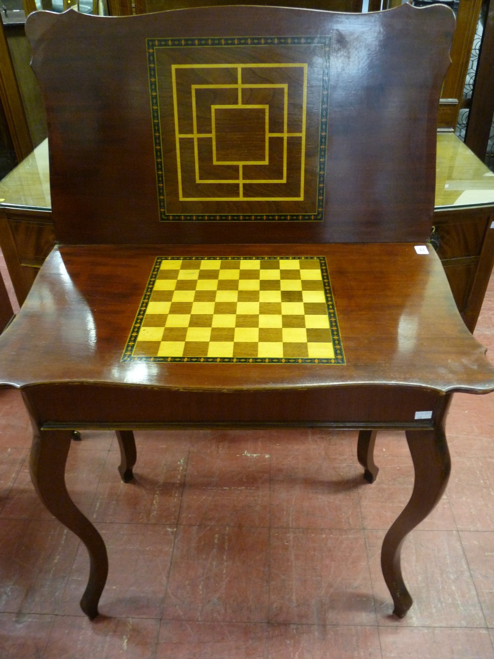 AN EDWARDIAN MAHOGANY FOLDOVER GAMES TABLE with line carved decoration to the shaped top and