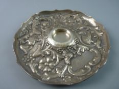 A CIRCULAR SILVER INK BOTTLE TRAY, heavily scrolled with raised flowers and leaves and with wavy