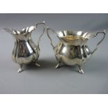 A SILVER CREAM JUG of waisted form with ridged decoration on four hoof supports and with a