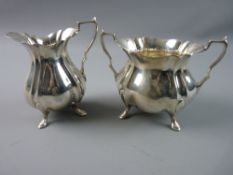 A SILVER CREAM JUG of waisted form with ridged decoration on four hoof supports and with a